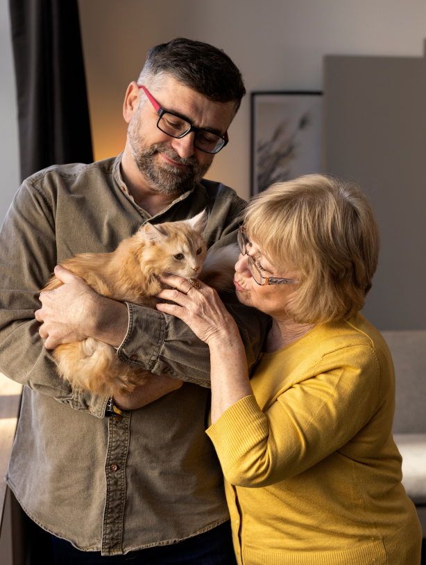 Older couple cuddling their fluffy orange cat in a warm living room