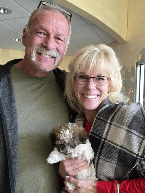 Smiling couple holding a small curly-haired puppy indoors